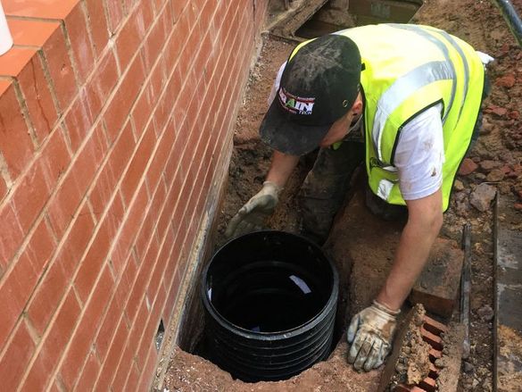 A man repairing a drain near a brick wall